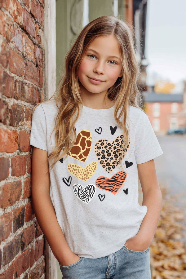Young girl wearing a white t-shirt with animal print hearts leaning against a brick wall.