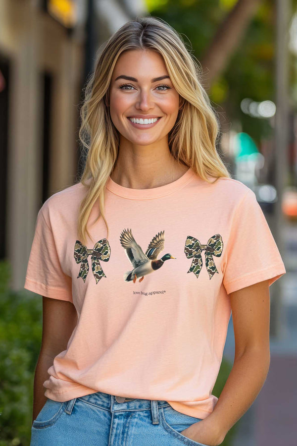 Woman wearing a peach t-shirt with duck and bow design on a city street.