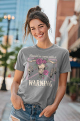Woman wearing a gray t-shirt with a graphic design and text, standing on a city street.