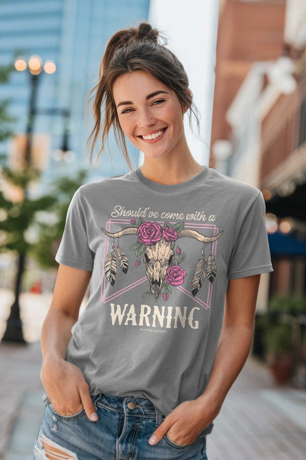 Woman wearing a gray t-shirt with a graphic design and text, standing on a city street.