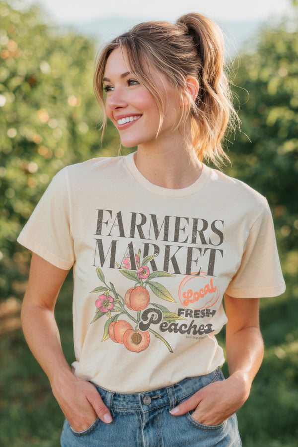 Woman wearing a 'Farmers Market Fresh Peaches' t-shirt in an orchard.