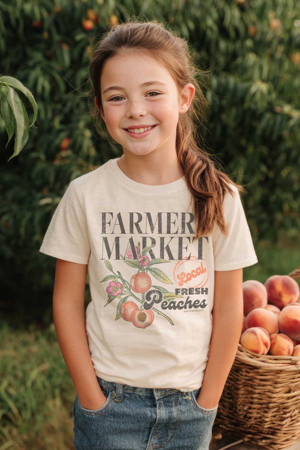 Young girl in a 'Farmer Market' t-shirt with a basket of peaches in an orchard.