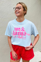 Person wearing a light blue t-shirt with pink text and red shorts against a beige wall.