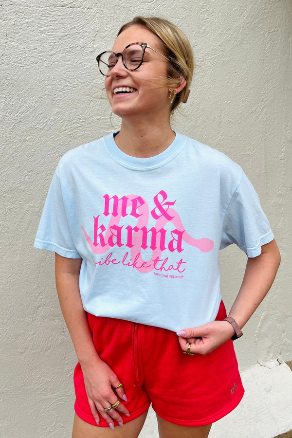 Person wearing a light blue t-shirt with pink text and red shorts against a beige wall.
