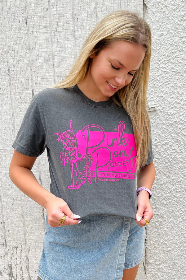 Woman wearing a gray t-shirt with pink graphic design against a textured wall.