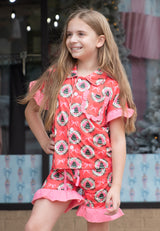 Young girl wearing a red and pink pajamas with a Christmas pattern in front of a decorative background.