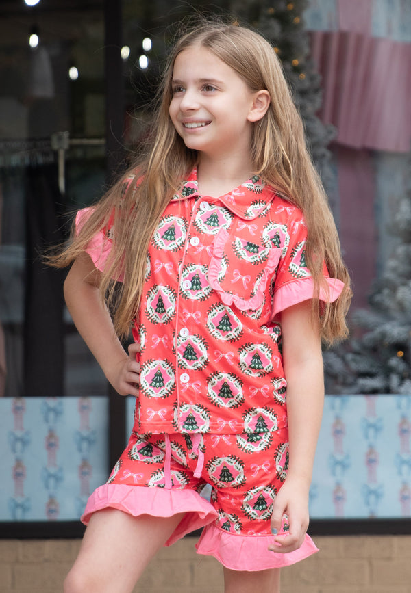 Young girl wearing a red and pink pajamas with a Christmas pattern in front of a decorative background.