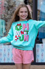 Young girl wearing a light blue sweatshirt with colorful text and pink shorts, standing in front of a store window display.