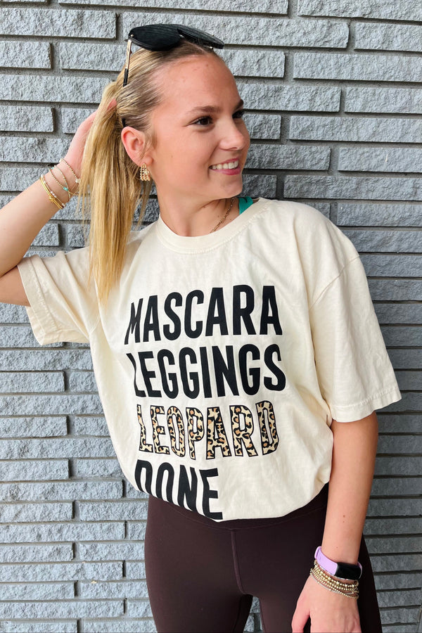 Woman wearing a cream t-shirt with text standing against a brick wall.
