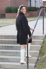 Woman in a black dress and white knee-high boots standing on steps outdoors.