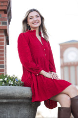 Woman in a red dress sitting outdoors with a blurred building in the background