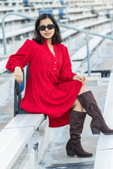 Woman in a red dress and brown knee-high boots sitting on bleachers.