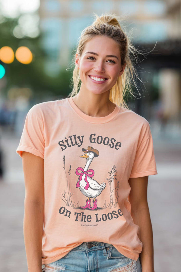 Woman wearing a peach t-shirt with a goose graphic and text, standing on a street.